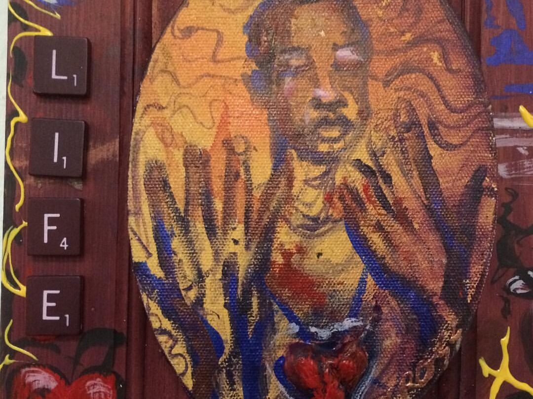 An oval painting shows a dark-skinned figure with closed eyes and raised hands in warm tones. Scrabble tiles spelling “LIFE” run vertically on the left. The background features hearts and swirling patterns in red, blue, and yellow hues.