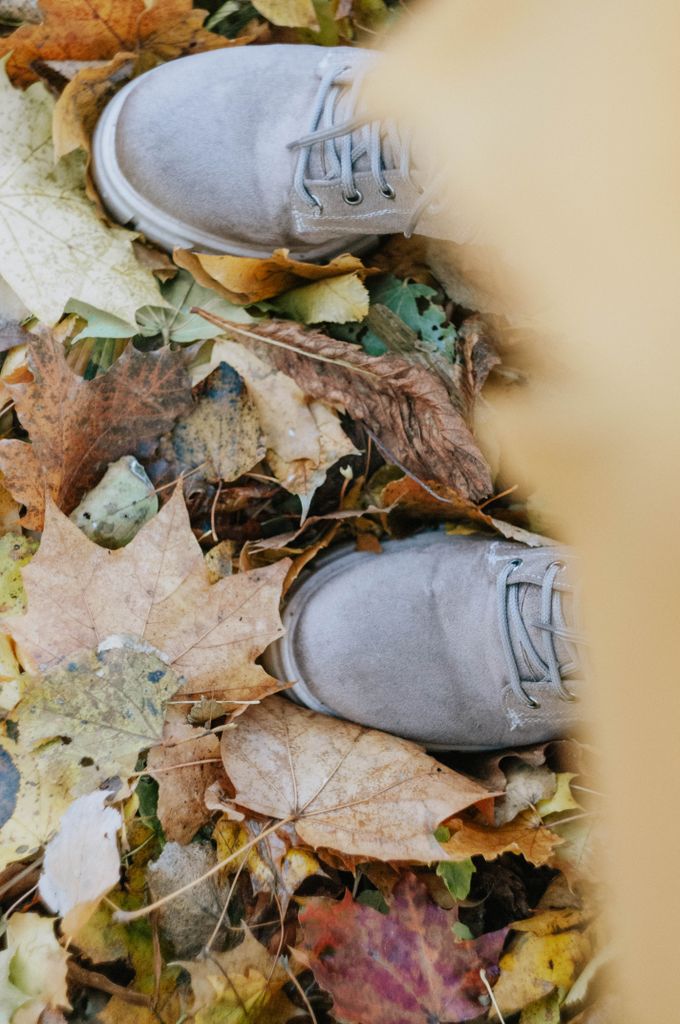 Close-up of gray shoes on colorful autumn leaves, capturing fall vibes.