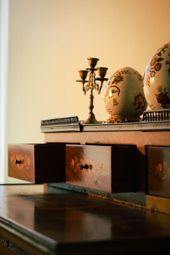 Elegant wooden dresser featuring ornamental eggs and vintage candleholder in warm lighting.